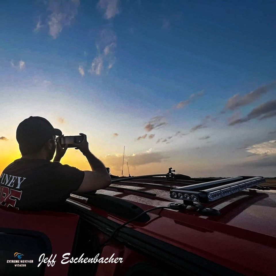 Storm Chaser Jeff Eschenbacker takes a photo of the sunset while standing on the footstep of his truck .