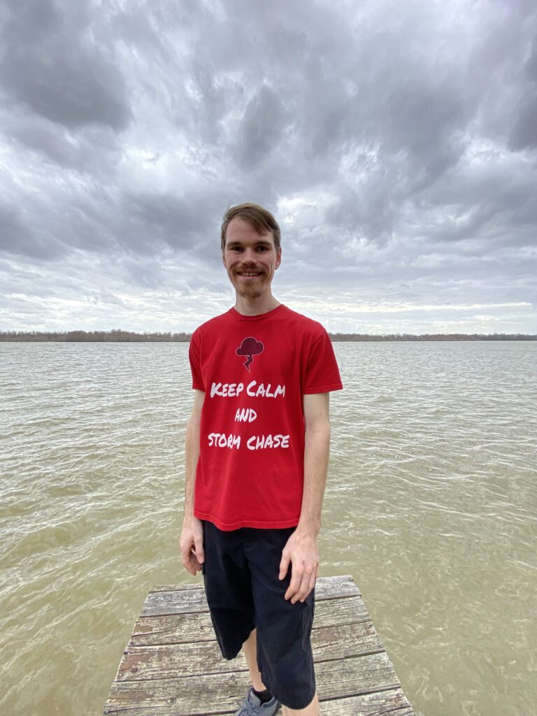 Joseph Pisani is standing on a dock wearing red t-shirt that reads keep calm and storm chase 
